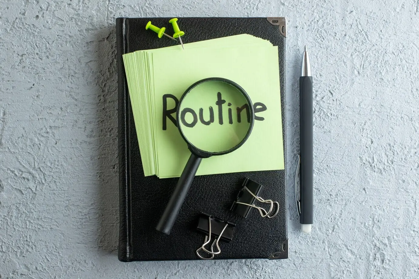 Вид сверху: написанная заметка о распорядке на зелёных стикерах, с блокнотом и лупой на белом фоне; колледж, работа, школа, офис, бизнес, тетрадь, цвет.